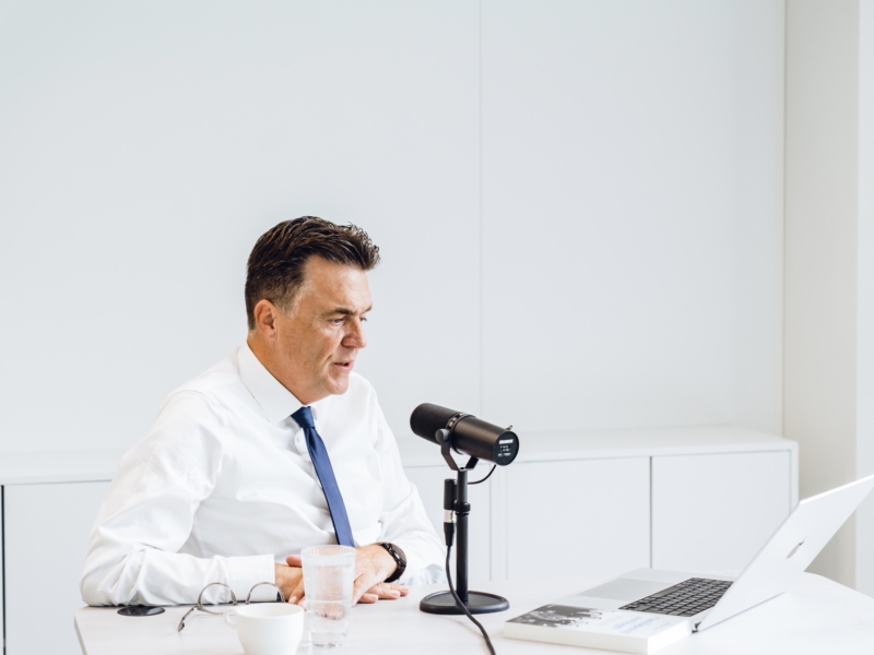 een man zit voor een microfoon en maakt dankzij 50 Koffies Producties een podcast