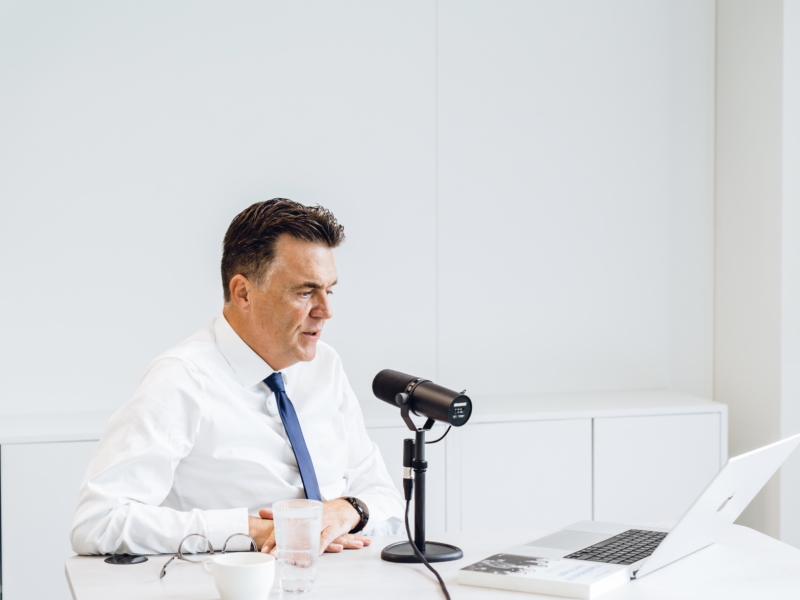 een man zit voor een microfoon en maakt dankzij 50 Koffies Producties een podcast