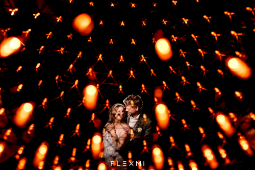 Bruidspaar voor een donkere achtergrond met allemaal lampjes rond hen heen