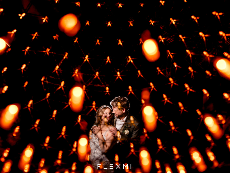 Bruidspaar voor een donkere achtergrond met allemaal lampjes rond hen heen