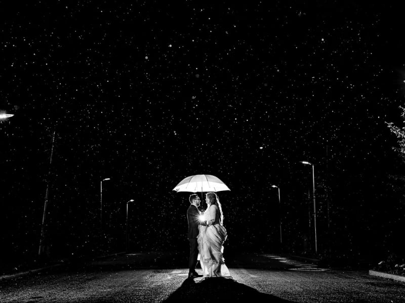 Bruidspaar staat onder een paraplu in de regen