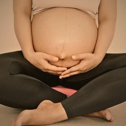 Zwangere vrouw in yogahouding met handen liefdevol rond haar buik, symbool voor prenatale zorg.