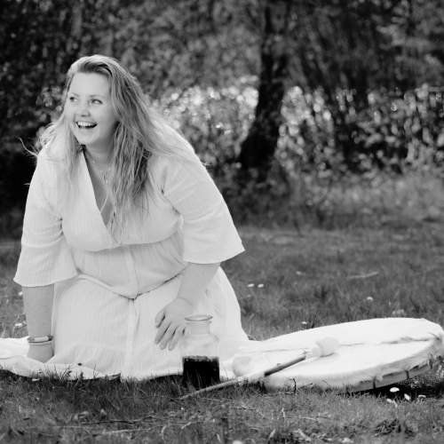 Vrouw op haar knieën op het gras, lacht en heeft een drum naast zich liggen
