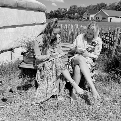 Twee vrouwen die naast elkaar op een bankje zitten en aan het schrijven zijn