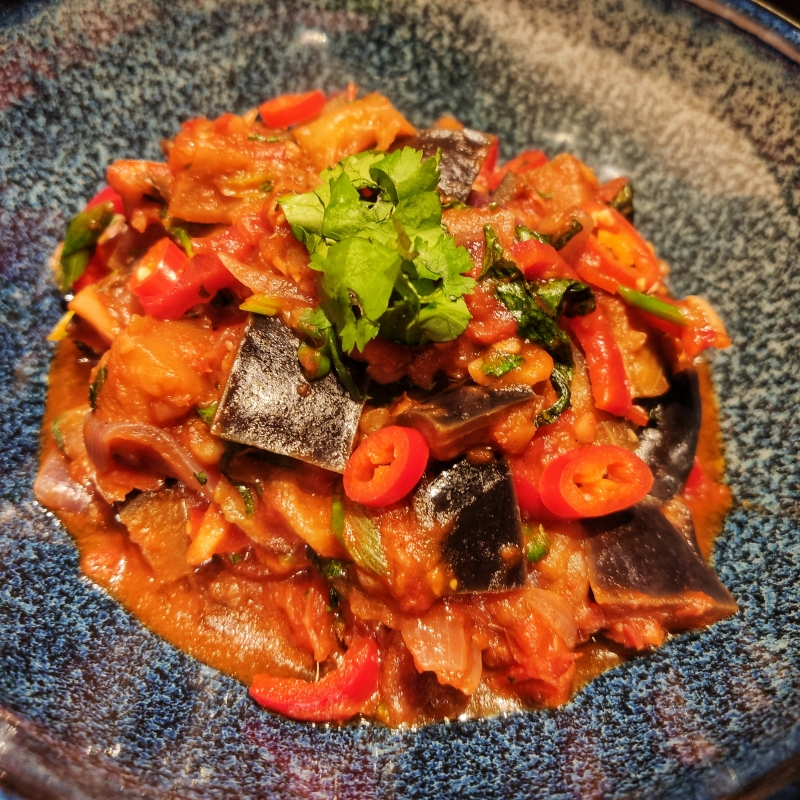 Ca Tim Kho To (Vietnamese gestoofde aubergine met tomaat) op een blauw bord met rijst