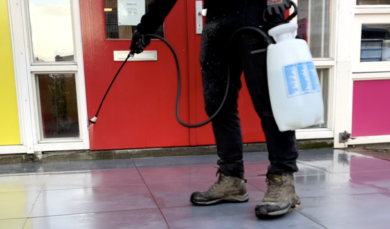 Marciano van De Antislip Expert brengt antislip vloeistof aan bij een entree van een school