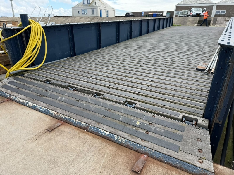 Stalen loopbrug met houten planken en antislipstrips bij de aansluiting op de kade
