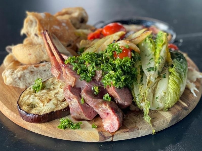 Lamskoteletten met chimichurri, gegrilde groenten en brood op een houten plank tijdens de BBQ workshop bij Bedstay op 8 in Dalen