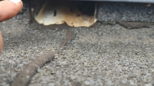 Close-up van een dakafvoer op een plat bitumen dak, met zichtbare scheuren en vuilophoping die lekkage kunnen veroorzaken.