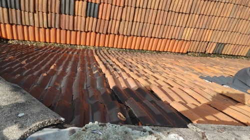 Hellend dak met verkleurde, gebroken en verschoven dakpannen — indicatie van veroudering en verhoogde kans op daklekkage.