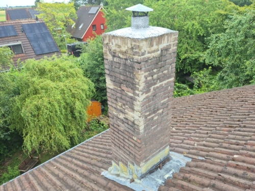 Vrijstaande schoorsteen op een pannendak met zichtbaar verouderd lood rondom de basis, wat kan leiden tot lekkage bij regenval.