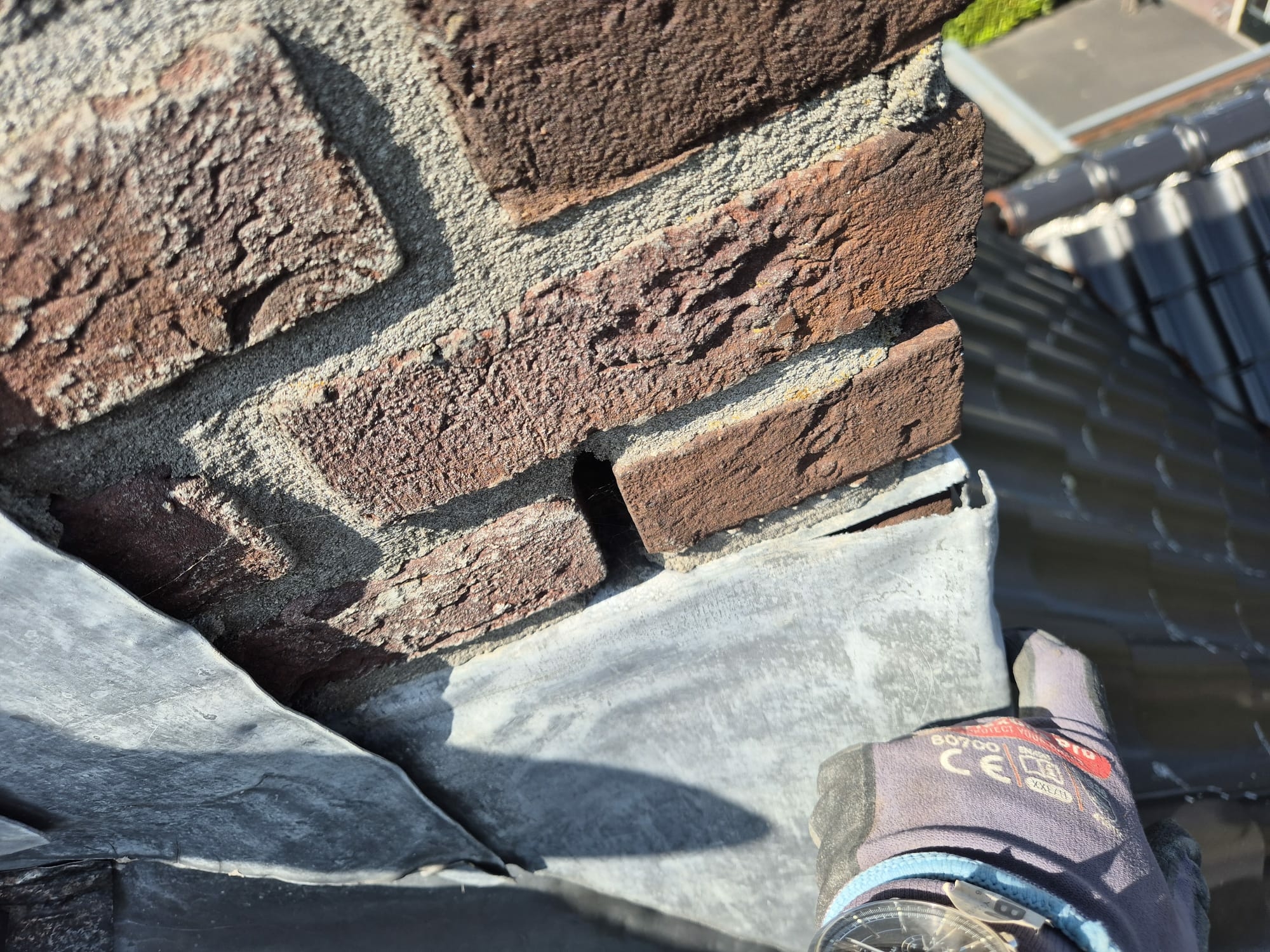 Bovenaanzicht van een lekkende schoorsteen met slecht aangebrachte loodslab en roetsporen.