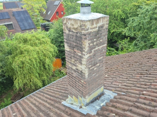 Vrijstaande schoorsteen op een pannendak met zichtbaar verouderd lood rondom de basis, wat kan leiden tot lekkage bij regenval.