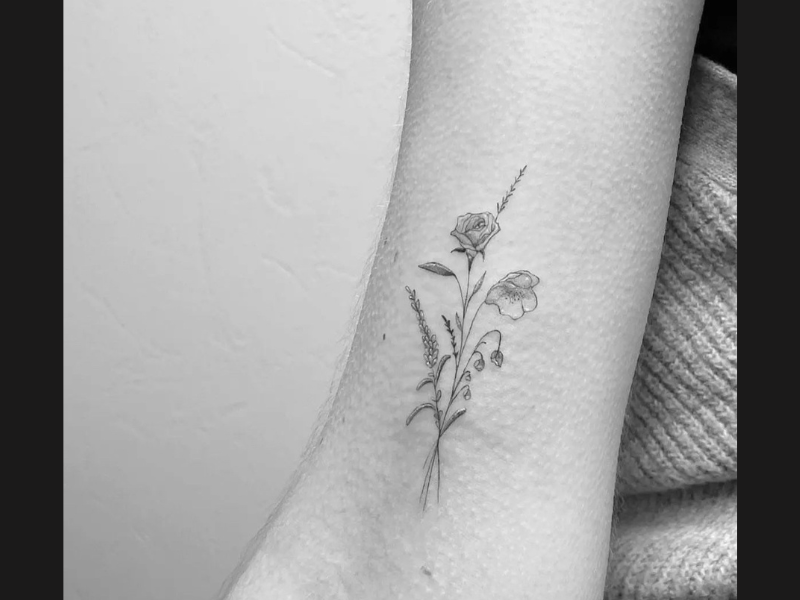 Fine line bloemen tattoo met roos op bovenarm