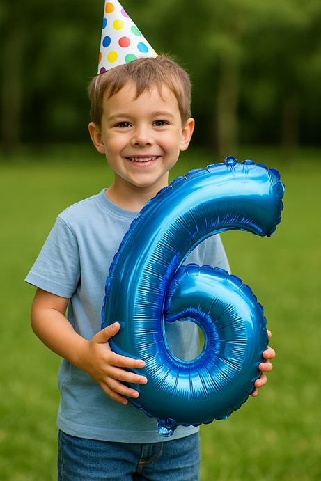 Zesjarige jongen lacht en houdt een grote blauwe ballon in de vorm van het cijfer 6 vast op een grasveld – inspiratie voor kinderfeestje 6 jaar
