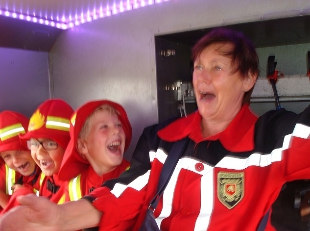 Kinderen in brandweerpak lachen in de brandweerauto – onderdeel van ons familiedag-arrangement met BBQ bij de brandweer in Heerewaarden (Gelderland). Veilig, verzorgd en superleuk voor alle leeftijden.