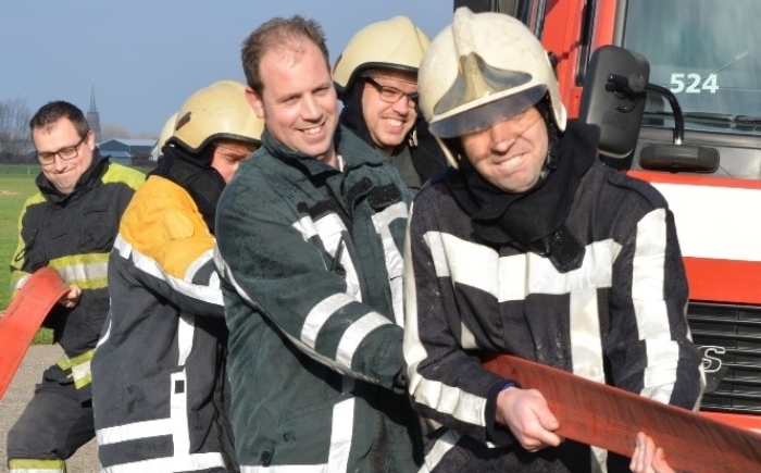 Volwassenen in brandweerpakken trekken als team aan een brandslang voor de brandweerauto tijdens het familiefeest arrangement; plezier en teamwork.