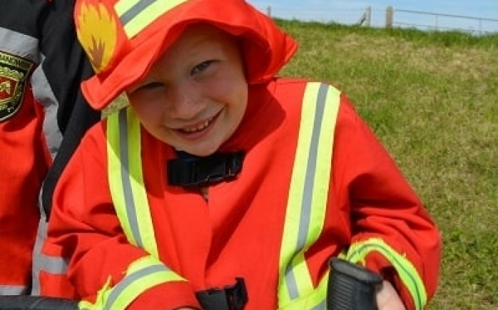 Klein kindje houdt trots de brandweerslang vast en lacht breed tijdens het familiedag arrangement met de échte brandweerauto.