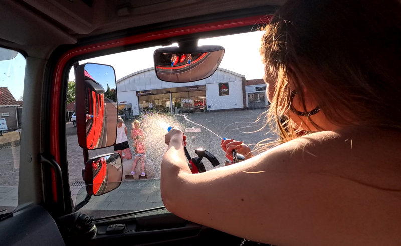 Deze foto toont een deelnemer die vanuit een echte brandweerauto een brandslang bedient. Brandweerauto.nu verzorgt unieke belevenissen, schoolgala vervoer, kinderfeestjes, bedrijfsuitjes en vrijgezellenfeesten in Brabant.