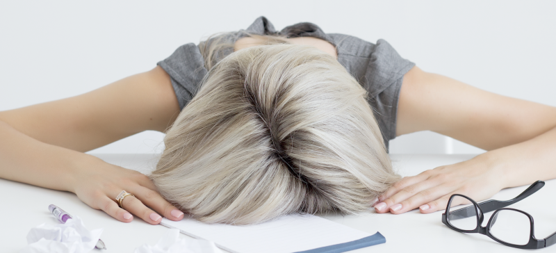 Vrouw moe met het haar hoofd op het bureau