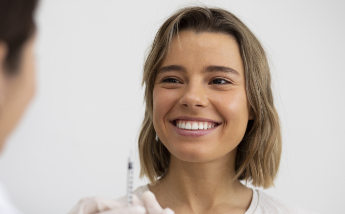Vrouw lacht ontspannen terwijl een botox behandeling in de bovenlip wordt uitgevoerd met een fijne naald voor gummy smile correctie