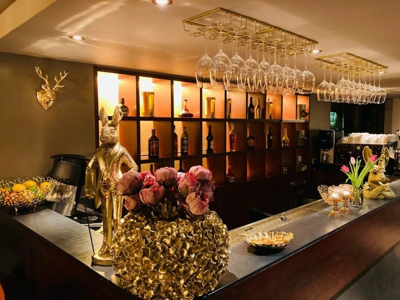 Sfeervol ingerichte bar met hangende wijnglazen, verlichte flessen en gouden decoratie in de borrelbistro van De La Frontière in Slenaken