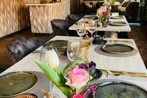 Stijlvol gedekte tafels met bloemen, gouden bestek en wijnglazen in de borrelbistro van De La Frontière Bed & Borrelbistro in Slenaken