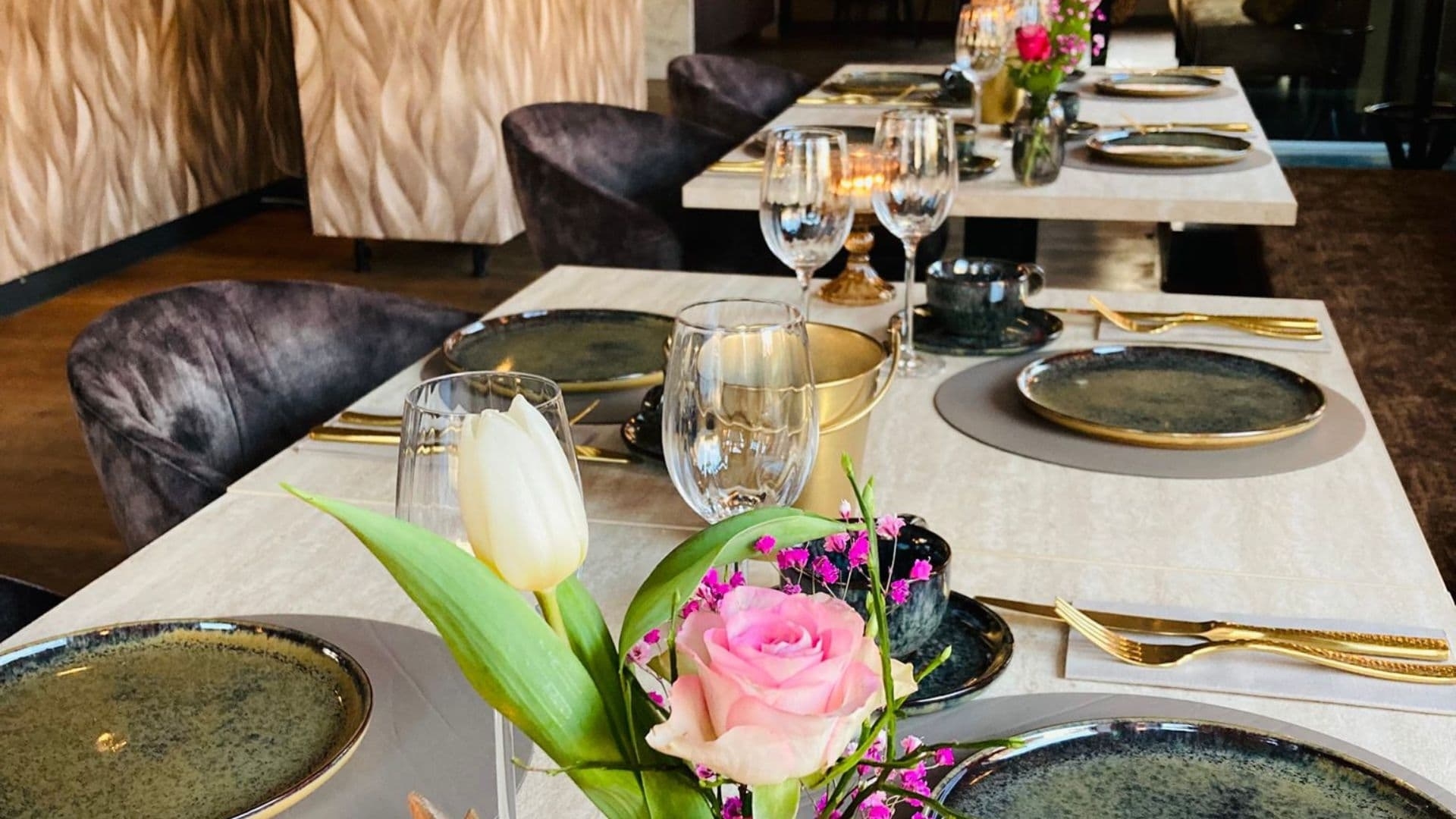 Sfeervolle gedekte tafels in de borrelbistro van De La Frontière in Slenaken Stijlvol gedekte tafels met bloemen, gouden bestek en wijnglazen in de borrelbistro van De La Frontière Bed & Borrelbistro in Slenaken