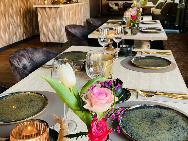 Stijlvol gedekte tafels met bloemen, gouden bestek en kaarslicht in de borrelbistro van De La Frontière Bed & Borrelbistro in Slenaken