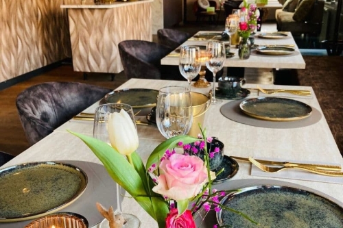 Luxe gedekte tafels met bloemen, kaarsen en gouden bestek in de borrelbistro van De La Frontière in Slenaken