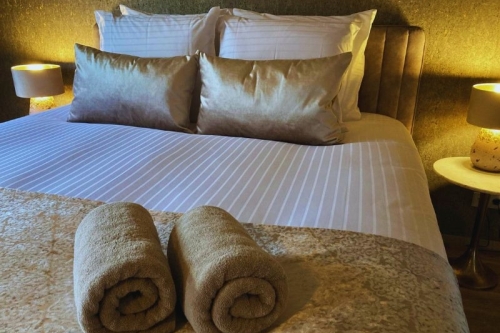 Sfeervol opgemaakt tweepersooonsbed met zachte handdoeken en warme sfeerverlichting in de knusse kamer van De La Frontière Bed & Borrelbistro in Slenaken