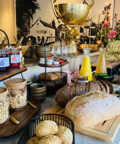 Rijkelijk gedekte ontbijttafel met vers brood, muesli, jam en vers sap bij De La Frontière Bed & Borrelbistro in Slenaken