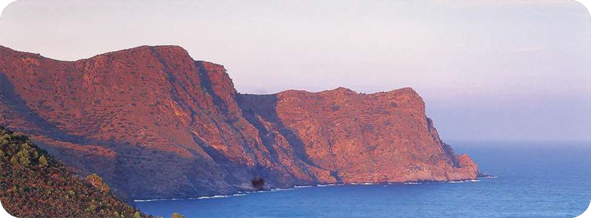 Zijaanzicht van de roodbruine, vulkanische kliffen van landtong Cap Norfeu in het natuurpark Cap de Creus, uitlopend in de blauwe Middellandse Zee.