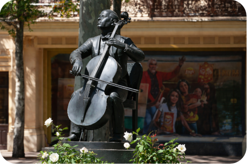 Een bronzen standbeeld van een zittende cellist Pau Casals die geconcentreerd op zijn instrument speelt, geplaatst op een sokkel in een buitenomgeving.