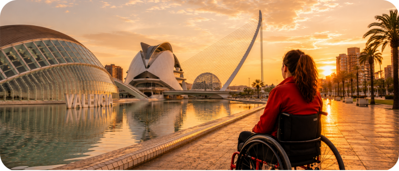 Een persoon in een rolstoel kijkt bij zonsondergang uit over de Ciudad de las Artes y las Ciencias in Valencia