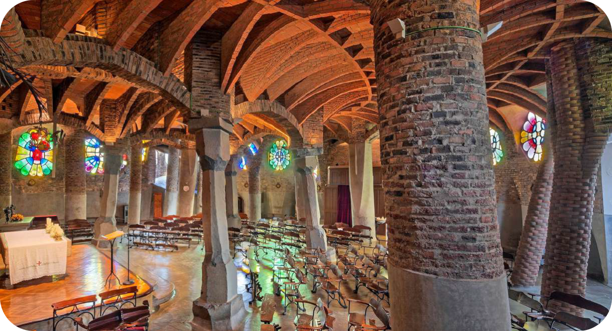 Interieur van de Cripta de la Colònia Güell van architect Antoni Gaudí, met schuine bakstenen kolommen, een gewelfd plafond en kleurrijke glas-in-loodramen