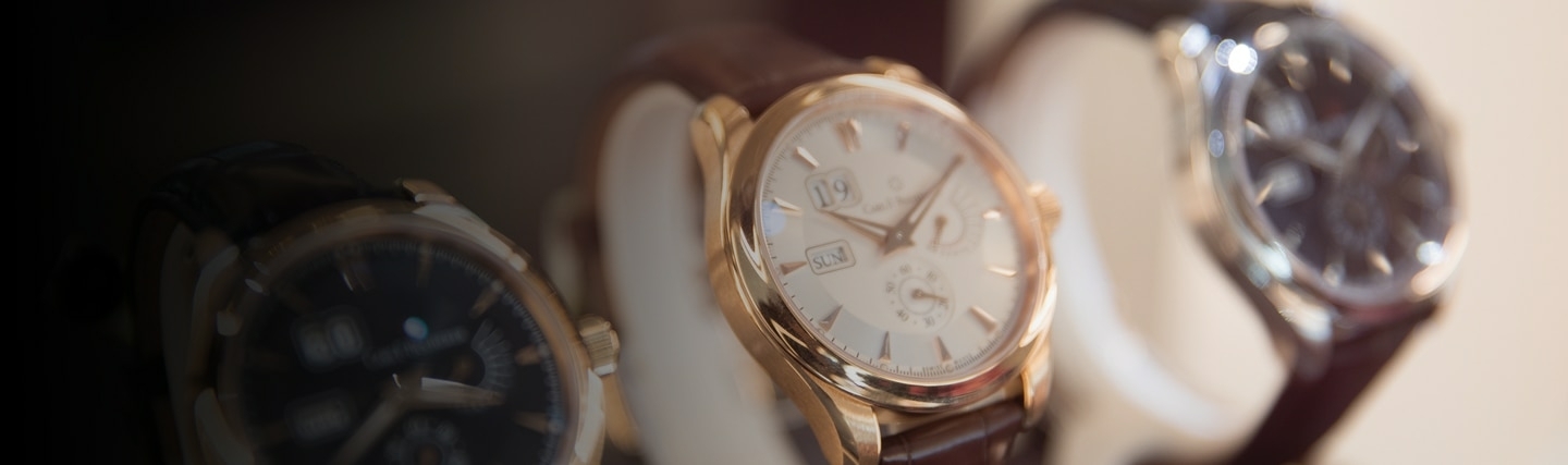 Close-up van luxe herenhorloges met lederen bandjes in een etalage, met goud- en zilverkleurige details en verfijnde wijzerplaten.