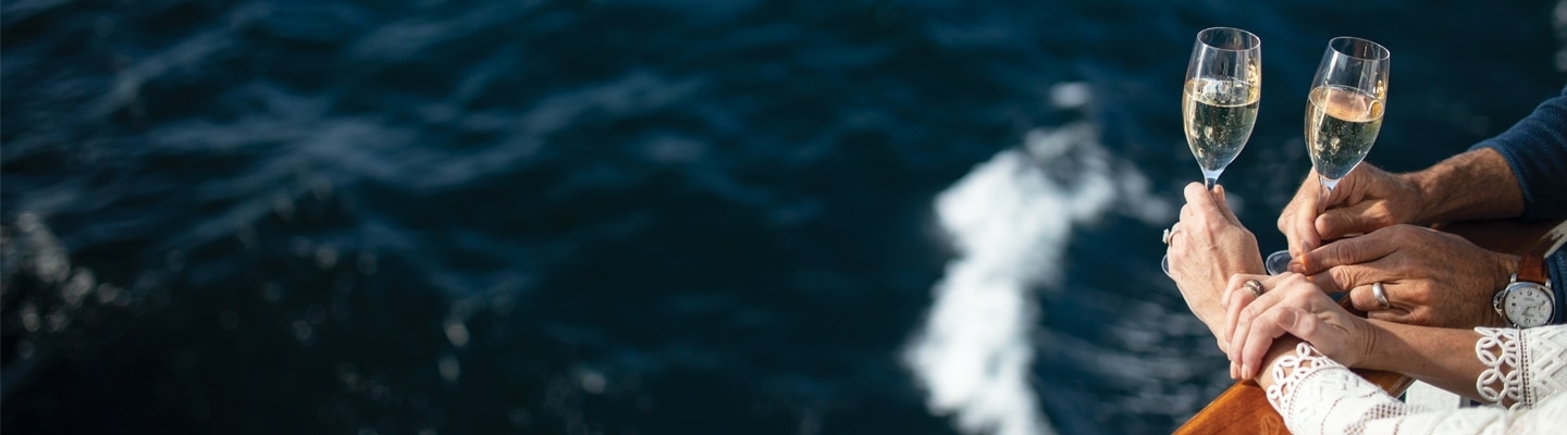 Twee personen heffen champagneglazen terwijl ze samen genieten van het uitzicht op zee vanaf het dek van een cruiseschip.