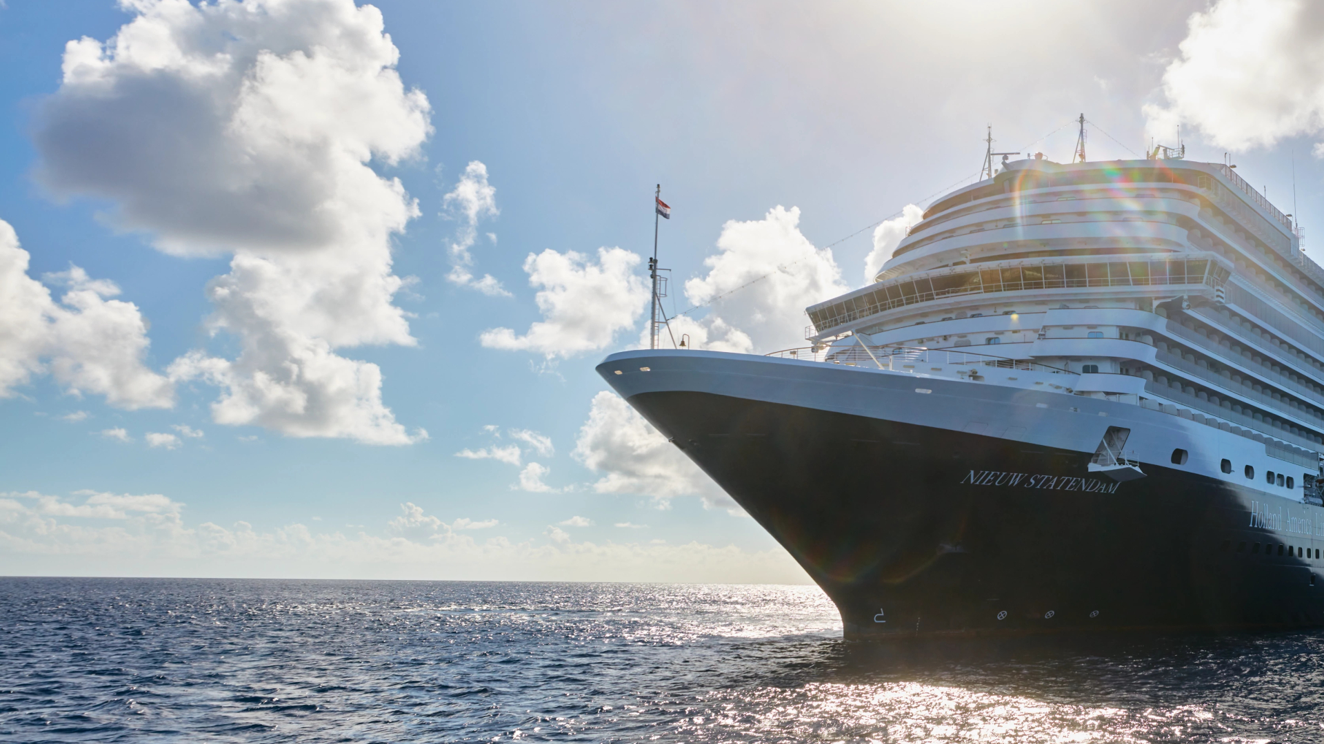 Alt tekst (140 tekens): Cruiseschip Nieuw Statendam van Holland America Line vaart op open zee onder een stralende zon en blauwe hemel met lichte wolken.