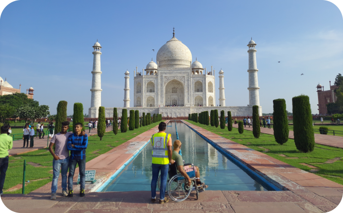 Een foto van de Taj Mahal in Agra, India, genomen vanaf de reflectiepool. Op de voorgrond staat een bezoeker in een rolstoel