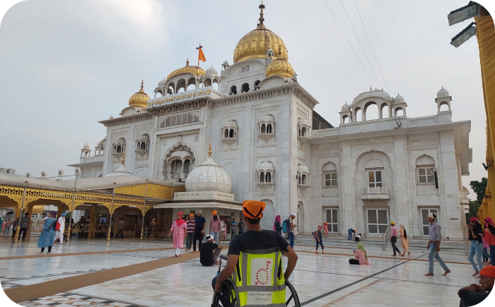 Een man in een rolstoel kijkt uit over de binnenplaats van de Gurdwara Bangla Sahib, een witmarmeren Sikh-tempel in New Delhi met glanzende gouden koepels.