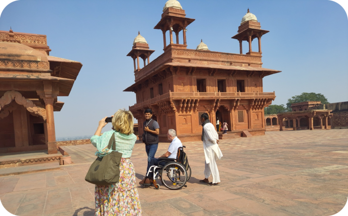 Rolstoel toeristen op een zonnig plein voor de rood zandstenen Diwan-i-Khas in Fatehpur Sikri, India, herkenbaar aan de vier koepelvormige paviljoens op het dak.