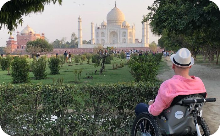 De afbeelding toont Max Burt, een rolstoelgebruiker, die geniet van het uitzicht op de Taj Mahal in India.