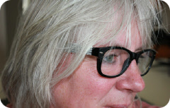 Een close-upfoto van een vrouw met grijs haar en een zwarte bril, van opzij gezien.