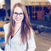 Een jonge vrouw met lang, steil, roodbruin haar en een bril met een donker montuur glimlacht naar de camera.