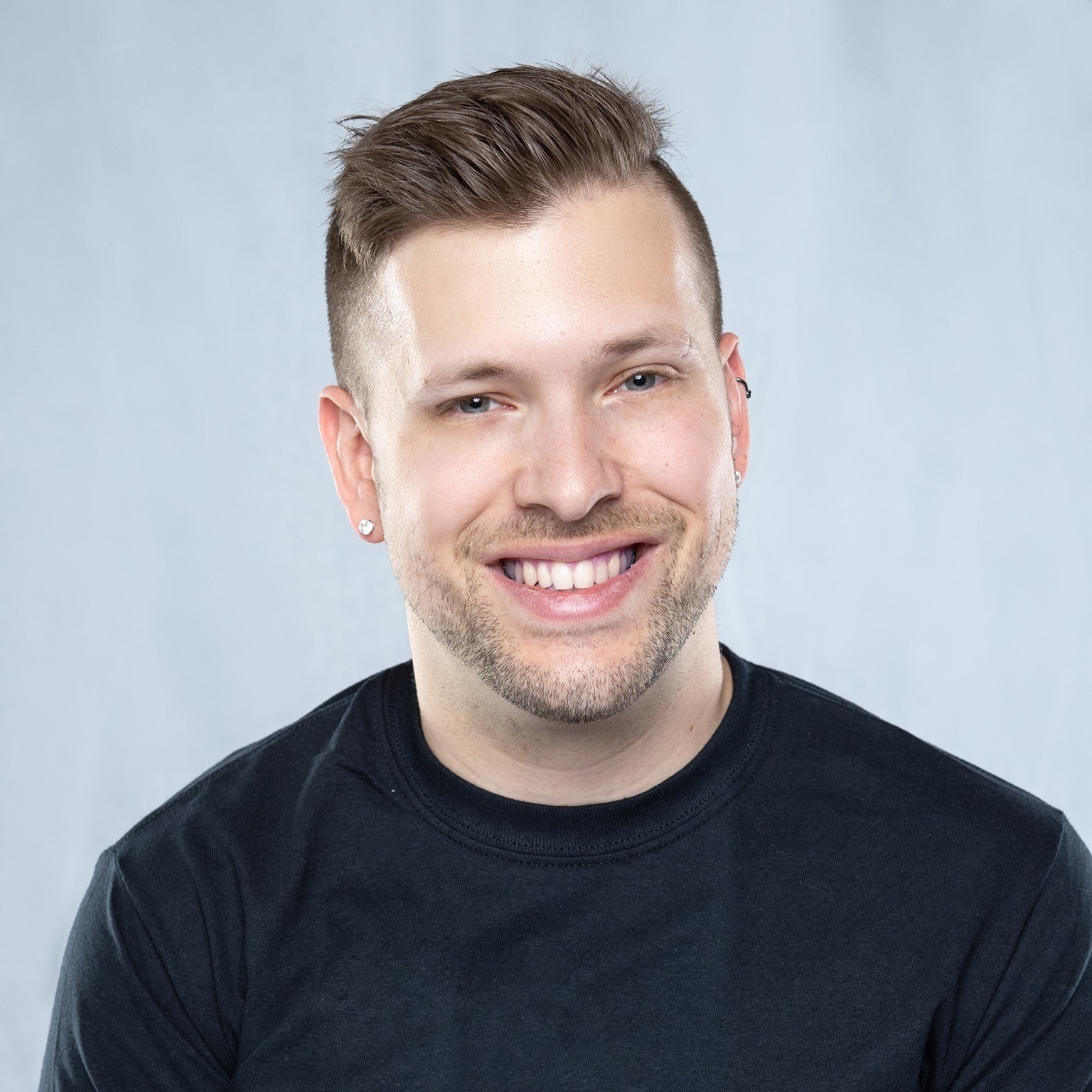 pasfoto van Marco Pasqua in zwarte trui beginnend baardje en zijn haar naar achteren gestyld