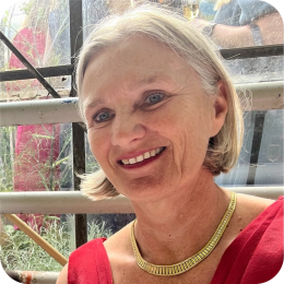 Een lachende vrouw met kort blond/grijs haar en een gouden ketting