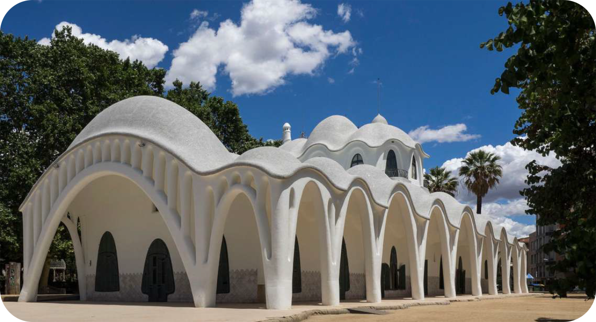 Wit modernistisch gebouw Masia Freixa in Terrassa met golvende daken en parabolische bogen onder een blauwe lucht met wolken.