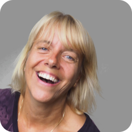 Een lachende vrouw met blond haar, die naar de camera kijkt.