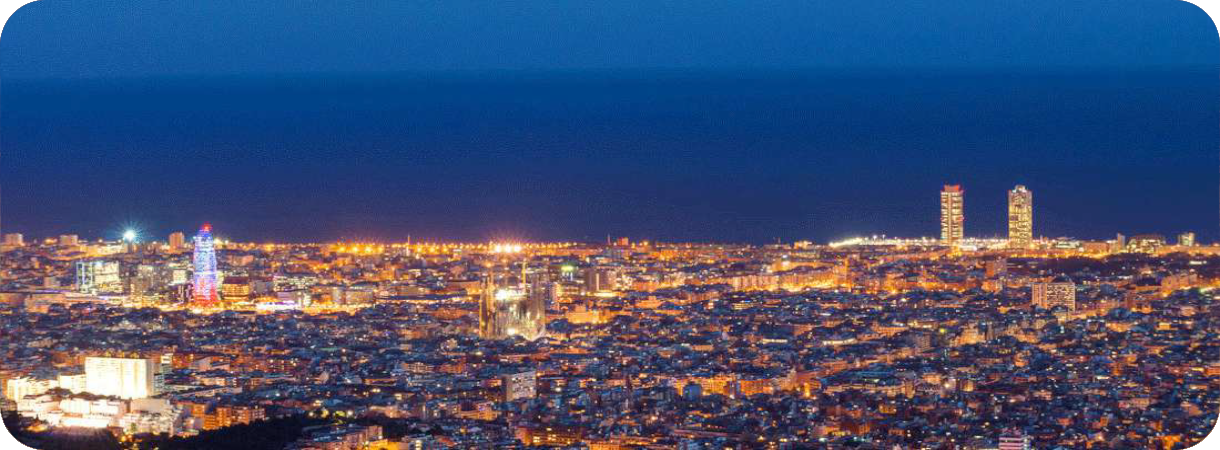 Panoramisch nachtzicht over de verlichte skyline van Barcelona met de Sagrada Família en Torre Glòries onder een donkerblauwe lucht.